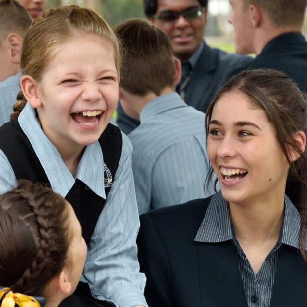 Two girls laughing together with a group of people in the background
